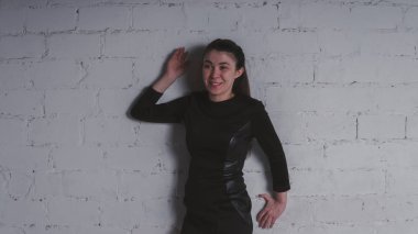 Kız beyaz duvara karşı poz. Siyah elbise modeli. Esmer Doğu görünüyor.