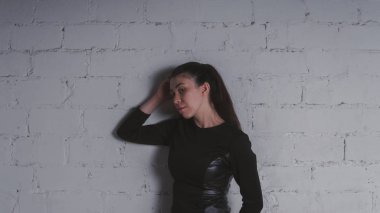 Kız beyaz duvara karşı poz. Siyah elbise modeli. Esmer Doğu görünüyor.