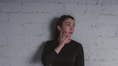 Kız beyaz duvara karşı poz. Siyah elbise modeli. Esmer Doğu görünüyor.