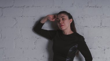 Kız beyaz duvara karşı poz. Siyah elbise modeli. Esmer Doğu görünüyor.