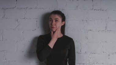 Kız beyaz duvara karşı poz. Siyah elbise modeli. Esmer Doğu görünüyor.