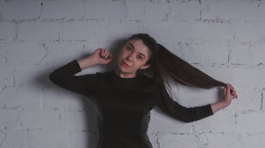 Kız beyaz duvara karşı poz. Siyah elbise modeli. Esmer Doğu görünüyor.