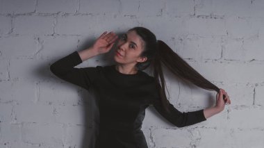 Kız beyaz duvara karşı poz. Siyah elbise modeli. Esmer Doğu görünüyor.