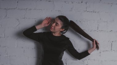 Kız beyaz duvara karşı poz. Siyah elbise modeli. Esmer Doğu görünüyor.