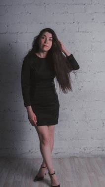 Kız beyaz duvara karşı poz. Siyah elbise modeli. Esmer Doğu görünüyor.