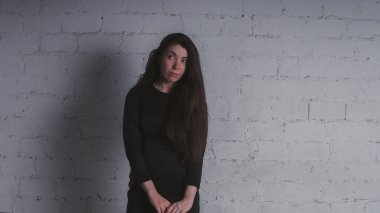 Kız beyaz duvara karşı poz. Siyah elbise modeli. Esmer Doğu görünüyor.
