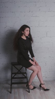 Kız beyaz duvara karşı poz. Siyah elbise modeli. Esmer Doğu görünüyor.