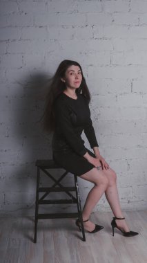 Kız beyaz duvara karşı poz. Siyah elbise modeli. Esmer Doğu görünüyor.