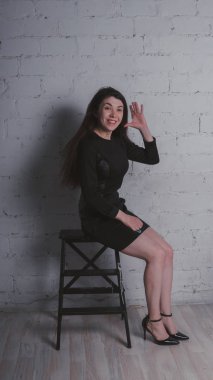 Kız beyaz duvara karşı poz. Siyah elbise modeli. Esmer Doğu görünüyor.