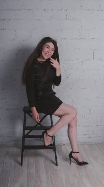 Kız beyaz duvara karşı poz. Siyah elbise modeli. Esmer Doğu görünüyor.