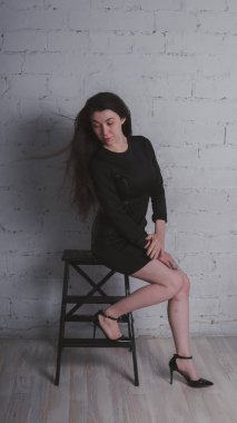 Kız beyaz duvara karşı poz. Siyah elbise modeli. Esmer Doğu görünüyor.
