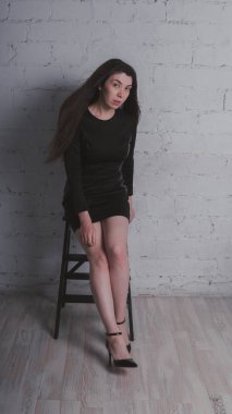 Kız beyaz duvara karşı poz. Siyah elbise modeli. Esmer Doğu görünüyor.