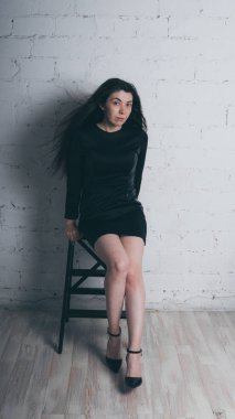 Kız beyaz duvara karşı poz. Siyah elbise modeli. Esmer Doğu görünüyor.