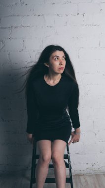 Kız beyaz duvara karşı poz. Siyah elbise modeli. Esmer Doğu görünüyor.