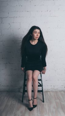 Kız beyaz duvara karşı poz. Siyah elbise modeli. Esmer Doğu görünüyor.