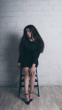 Kız beyaz duvara karşı poz. Siyah elbise modeli. Esmer Doğu görünüyor.