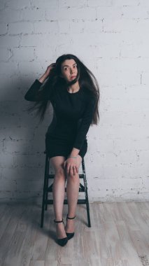 Kız beyaz duvara karşı poz. Siyah elbise modeli. Esmer Doğu görünüyor.