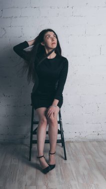 Kız beyaz duvara karşı poz. Siyah elbise modeli. Esmer Doğu görünüyor.