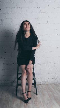 Kız beyaz duvara karşı poz. Siyah elbise modeli. Esmer Doğu görünüyor.