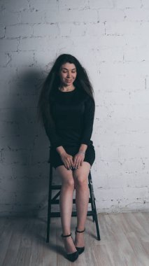 Kız beyaz duvara karşı poz. Siyah elbise modeli. Esmer Doğu görünüyor.