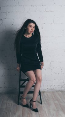 Kız beyaz duvara karşı poz. Siyah elbise modeli. Esmer Doğu görünüyor.