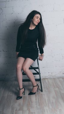 Kız beyaz duvara karşı poz. Siyah elbise modeli. Esmer Doğu görünüyor.