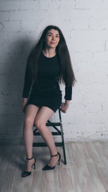 Kız beyaz duvara karşı poz. Siyah elbise modeli. Esmer Doğu görünüyor.