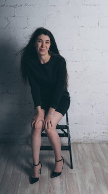 Kız beyaz duvara karşı poz. Siyah elbise modeli. Esmer Doğu görünüyor.