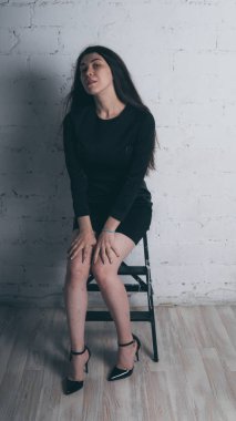 Kız beyaz duvara karşı poz. Siyah elbise modeli. Esmer Doğu görünüyor.