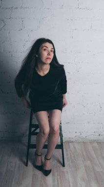 Kız beyaz duvara karşı poz. Siyah elbise modeli. Esmer Doğu görünüyor.