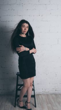 Kız beyaz duvara karşı poz. Siyah elbise modeli. Esmer Doğu görünüyor.