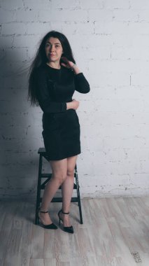 Kız beyaz duvara karşı poz. Siyah elbise modeli. Esmer Doğu görünüyor.