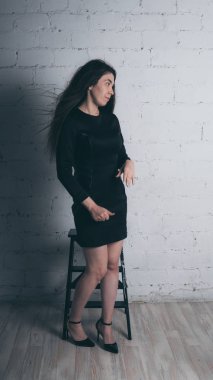 Kız beyaz duvara karşı poz. Siyah elbise modeli. Esmer Doğu görünüyor.