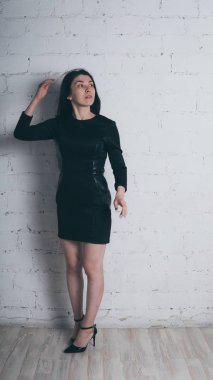 Kız beyaz duvara karşı poz. Siyah elbise modeli. Esmer Doğu görünüyor.