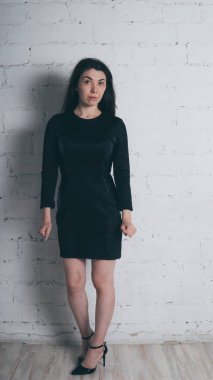 Kız beyaz duvara karşı poz. Siyah elbise modeli. Esmer Doğu görünüyor.