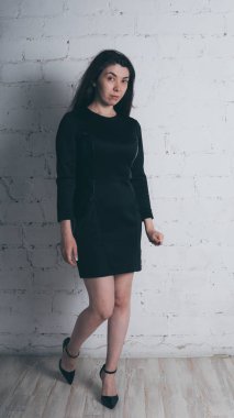 Kız beyaz duvara karşı poz. Siyah elbise modeli. Esmer Doğu görünüyor.