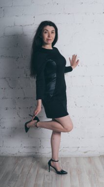 Kız beyaz duvara karşı poz. Siyah elbise modeli. Esmer Doğu görünüyor.