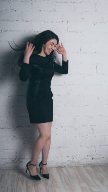 Kız beyaz duvara karşı poz. Siyah elbise modeli. Esmer Doğu görünüyor.