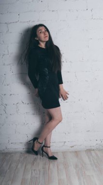 Kız beyaz duvara karşı poz. Siyah elbise modeli. Esmer Doğu görünüyor.