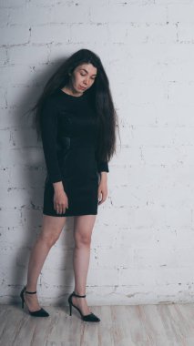 Kız beyaz duvara karşı poz. Siyah elbise modeli. Esmer Doğu görünüyor.