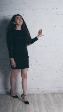 Kız beyaz duvara karşı poz. Siyah elbise modeli. Esmer Doğu görünüyor.