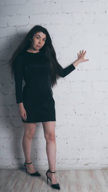 Kız beyaz duvara karşı poz. Siyah elbise modeli. Esmer Doğu görünüyor.