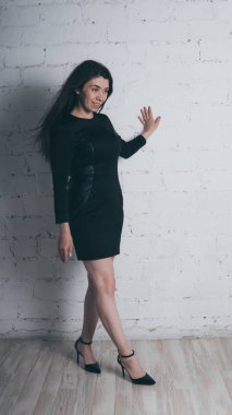 Kız beyaz duvara karşı poz. Siyah elbise modeli. Esmer Doğu görünüyor.