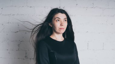 Kız beyaz duvara karşı poz. Siyah elbise modeli. Esmer Doğu görünüyor.