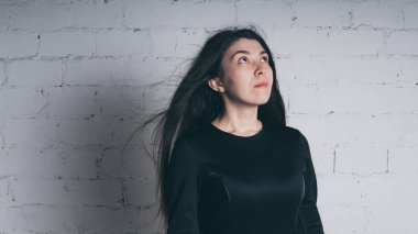 Kız beyaz duvara karşı poz. Siyah elbise modeli. Esmer Doğu görünüyor.