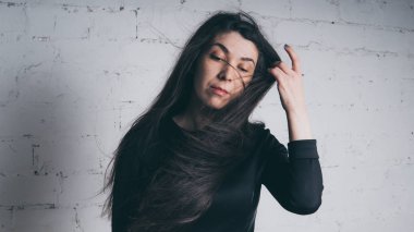 Kız beyaz duvara karşı poz. Siyah elbise modeli. Esmer Doğu görünüyor.