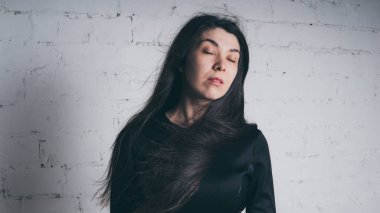 Kız beyaz duvara karşı poz. Siyah elbise modeli. Esmer Doğu görünüyor.