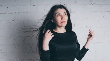 Kız beyaz duvara karşı poz. Siyah elbise modeli. Esmer Doğu görünüyor.