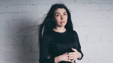 Kız beyaz duvara karşı poz. Siyah elbise modeli. Esmer Doğu görünüyor.