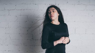 Kız beyaz duvara karşı poz. Siyah elbise modeli. Esmer Doğu görünüyor.